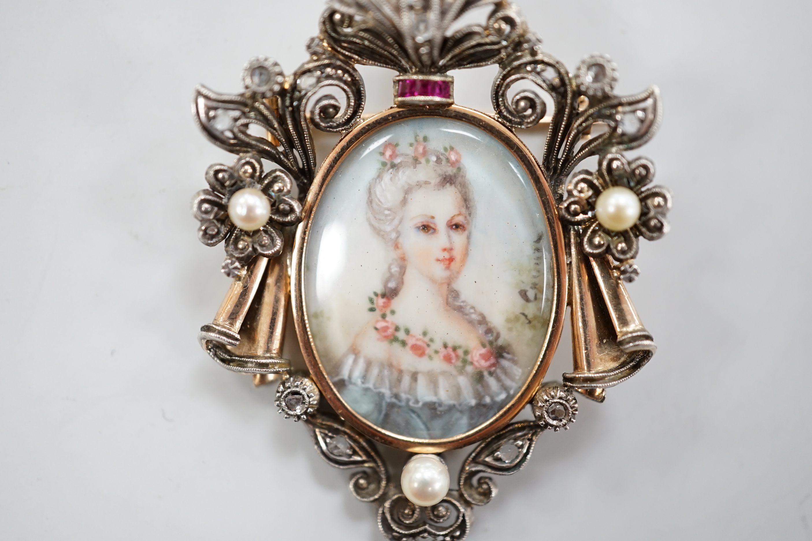 A late 19th/early 20th century continental yellow metal, seed pearl, ruby and diamond mounted pendant brooch, with inset oval miniature watercolour of a lady, indistinctly signed, 47mm, gross weight 10 grams., CITES Subm